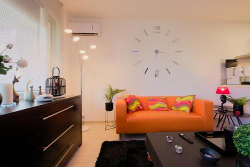 an orange couch in a living room with a clock on the wall at Bilocale Luxury fronte Ospedale in Udine
