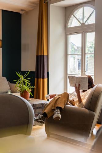 a woman laying on a couch reading a book at Hôtel Le D'Avaugour in Dinan