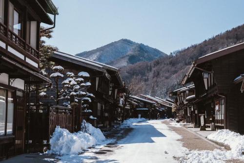 a snow covered street with buildings and a mountain at LA TERRA narai in Shiojiri