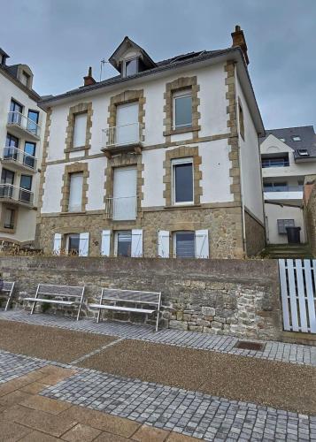 un bâtiment avec deux bancs devant lui dans l'établissement Appartement vue mer, Centre-ville & plage, à Quiberon