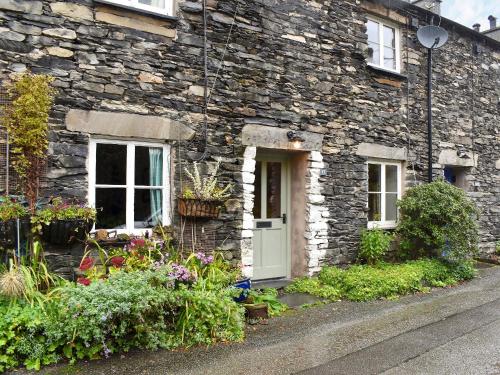 a stone house with a white door and flowers at The Burrow in Haverthwaite