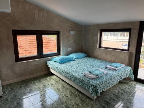 a bedroom with a bed with blue pillows and two windows at Къща за Гости Морска звезда in Ahtopol