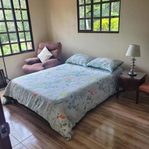 a bedroom with a bed and a chair and windows at Casa Bella Campestre in Guayabal de Síquima