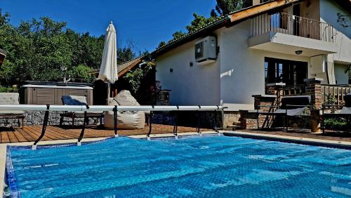 a swimming pool with a umbrella and a house at СПА къща за гости Каза Роза - Swiss Style Chalet Casa Rosa SPA Guest House in Kyustendil