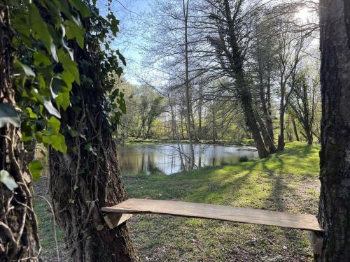 a wooden bench sitting between two trees in front of a river at cabane ô domaine södjé in Saint-Yrieix-sous-Aixe