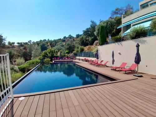 - une piscine avec des chaises sur une terrasse en bois dans l'établissement Duplex avec terrasse & vue dégagée dans domaine privé à Mandelieu, à Mandelieu-la-Napoule