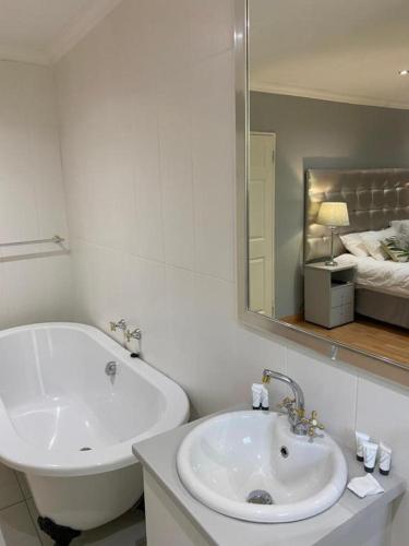 a bathroom with a sink and a tub and a mirror at Boutique at milner guesthouse in Bloemfontein