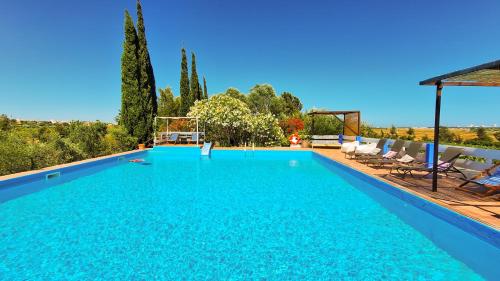 a large blue swimming pool with chairs and trees at Quinta da Fornalha - Santuario Agroecologico in Castro Marim
