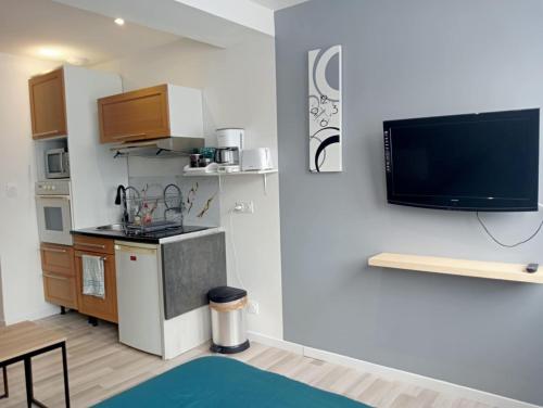 a living room with a kitchen and a tv on a wall at Grand studio centre-ville in Villedieu-les-Poëles