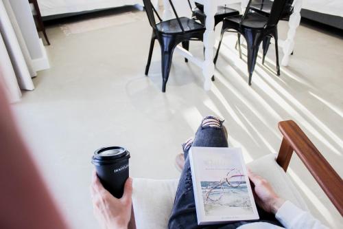 a person sitting on a chair with a book and a cup of coffee at Hartshuijs in Beaufort West