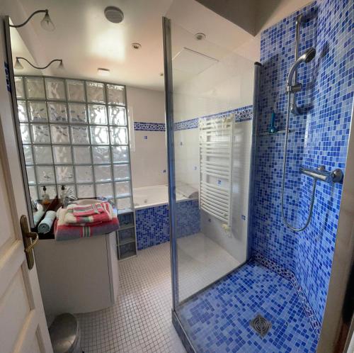 La salle de bains est pourvue de carrelage bleu, d'une douche et d'une baignoire. dans l'établissement La traboule, à La Tranche-sur-Mer