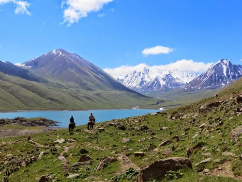 two people riding horses on a hill near a lake at Guest House Nur in Kochkor