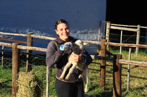 a woman holding a baby lamb with a bottle at Ganora Guest Farm, Camping and Excursions in Nieu-Bethesda