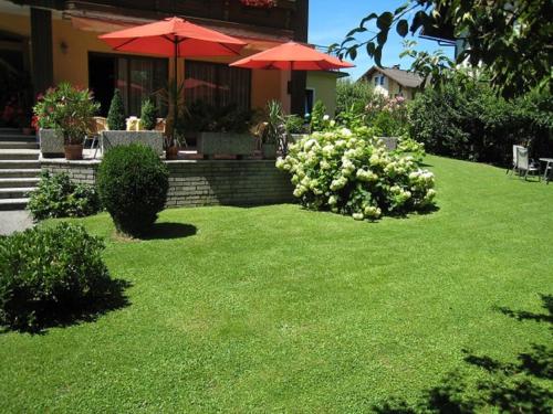 a yard with green grass and red umbrellas in front of a house at Strandpension Liane in Sankt Kanzian