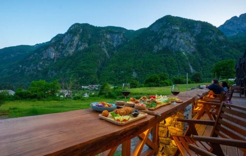 a wooden table with food and wine glasses and mountains at Hotel Restaurant Alpet Theth in Theth