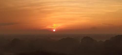 a sunset with the sun in the sky over trees at Cuti de Gold Coast Morib in Banting