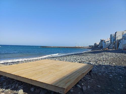 a wooden bench on a beach next to the water at Guesthouse El arca de Noé in Pozo Izquierdo