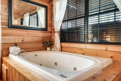 a white tub in a wooden bathroom with a window at Kate's Cabin - 3 min to Dollywood! Cabin with Hot tub, Game Room, and Resort Pool! in Sevierville