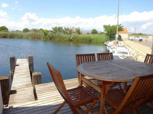 une terrasse en bois avec une table et des chaises à côté d'une rivière dans l'établissement Villa T4 vue lac avec ponton privé au Barcares - FR-1-782-80, au Barcarès