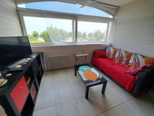 - un salon avec un canapé rouge et une grande fenêtre dans l'établissement Logement avec mezzanine, parking privé - Marseillan-Plage - FR-1-326-866, à Marseillan