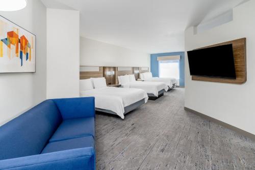 a hotel room with a blue couch and a flat screen tv at Holiday Inn Express & Suites Denver North - Thornton by IHG in Thornton