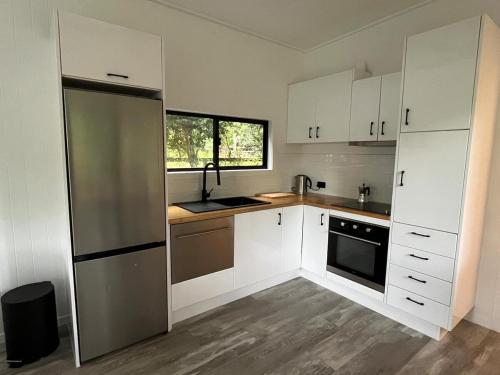 a kitchen with white cabinets and a stainless steel refrigerator at Cute and cosy 1 bedroom cabin in Mooloolah