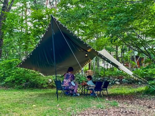 a woman and child sitting in chairs under a large umbrella at Hakuba Riverside Loghouse in Hakuba