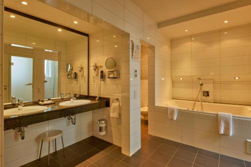 a bathroom with two sinks and a tub and a mirror at Trip Inn Hotel Esplanade, Düsseldorf in Düsseldorf