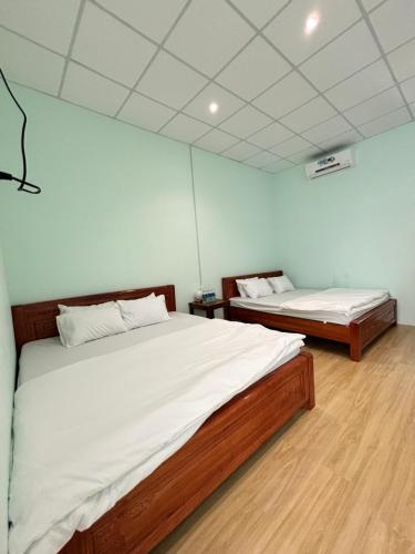 two beds in a room with white walls and wooden floors at Phan Lê Homestay in Ninh Hải
