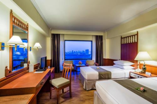a hotel room with two beds and a desk at Bangkok Palace Hotel in Bangkok