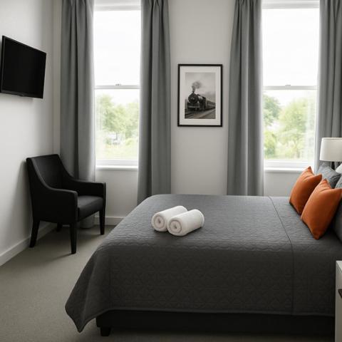 a bedroom with a bed and a chair and windows at The Old Railway Hotel Lumsden in Lumsden
