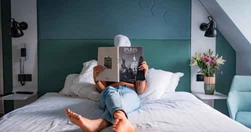 een persoon die op een bed ligt en een boek leest bij Hôtel Vendome Saint-Germain in Parijs
