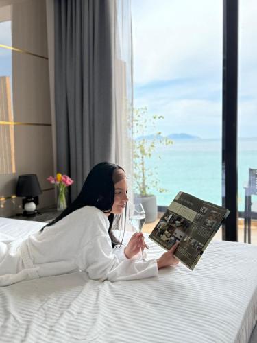 a woman laying on a bed with a book and a glass of wine at Belvedere Hotel & SPA in Vlorë