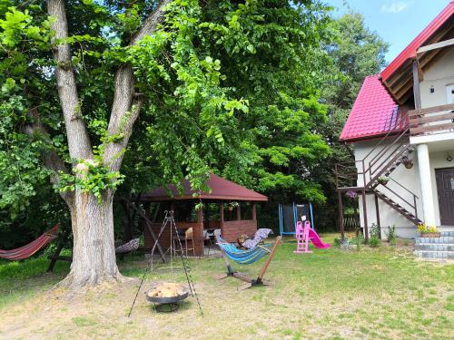 a yard with a tree and a hammock and a house at Agroturystyka Zacisze nad Pilicą in Stromiec