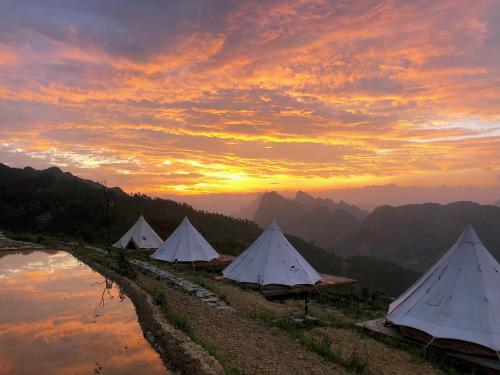 a group of white tents on a hill at sunset at Sunrise Ha Giang Camping An Introspective Stay in Suy Tung Su