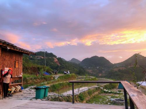 a woman standing next to a building with a view of a mountain at Sunrise Ha Giang Camping An Introspective Stay in Suy Tung Su