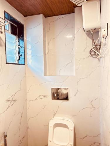 a white bathroom with a toilet and a window at Prince NX Hotel in Thane