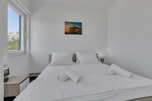 a white bedroom with two beds and a window at Villa la Perla in Baška Voda