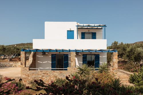 a white house with blue windows and bushes at Aurea Blu studio 15 Pure nature, relaxation, sea and sun in Aliko Beach