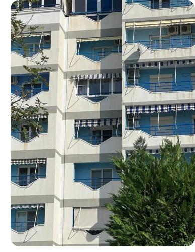 an apartment building with blue windows and a tree at Brecani Apartment in Shëngjin