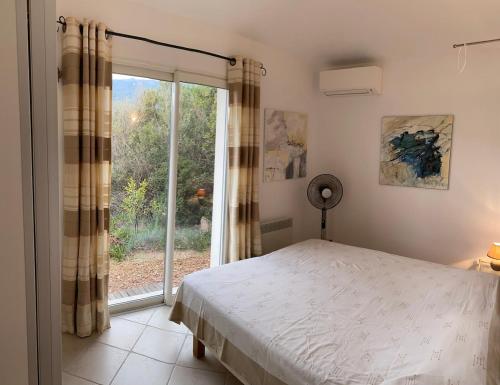 a bedroom with a bed and a large window at Maison récente entre mer et montagne in Figari