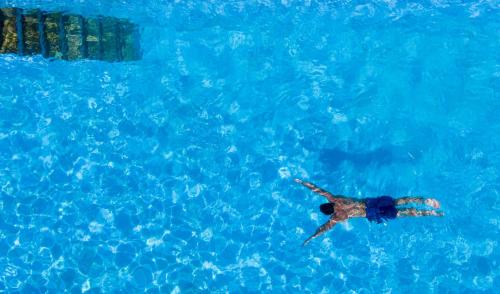 a man swimming in a pool of blue water at Hôtel Le Provençal - Rénové en 2025 - Bord de Mer in Hyères