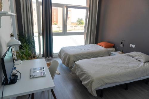 a hotel room with two beds and a desk and a television at Banama Coliving & Coworking, Surf & Yoga - Casa Roja in Corralejo