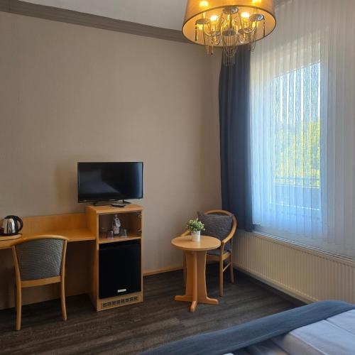 a room with a desk with a television and a table with chairs at Hotel am Kurpark in Bad Lauterberg