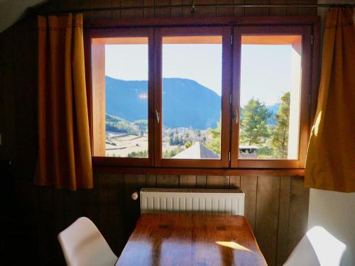 Cette chambre dispose d'une table en bois et de deux fenêtres. dans l'établissement Ecogite Mercantour Ô Perché, à La Colmiane