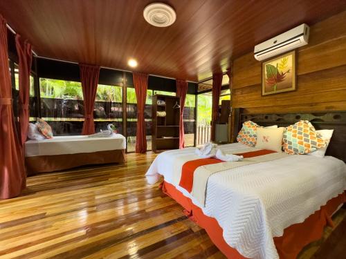 two beds in a room with wooden floors and windows at Hotel Heliconias Nature Inn & Hot Springs in Fortuna