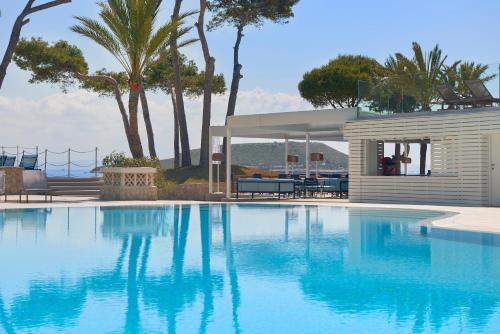 a swimming pool in front of a house with palm trees at Meliá Calviá Beach in Magaluf