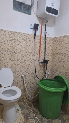 a bathroom with a toilet and a green bucket at 88HappyHomestay in Luwuk