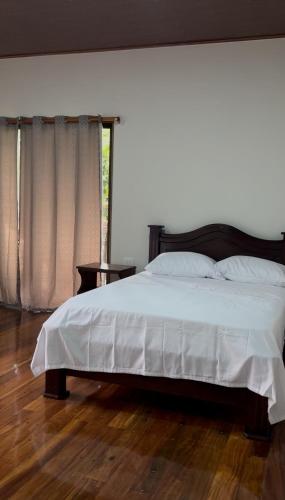 a bedroom with a bed with white sheets and a window at Chato Arenal Lodge in Fortuna