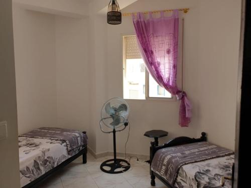 a bedroom with two beds and a window with a fan at APPARTEMENT AL HOCEIMA prés de PLAGE CALABONITA in Al Hoceïma